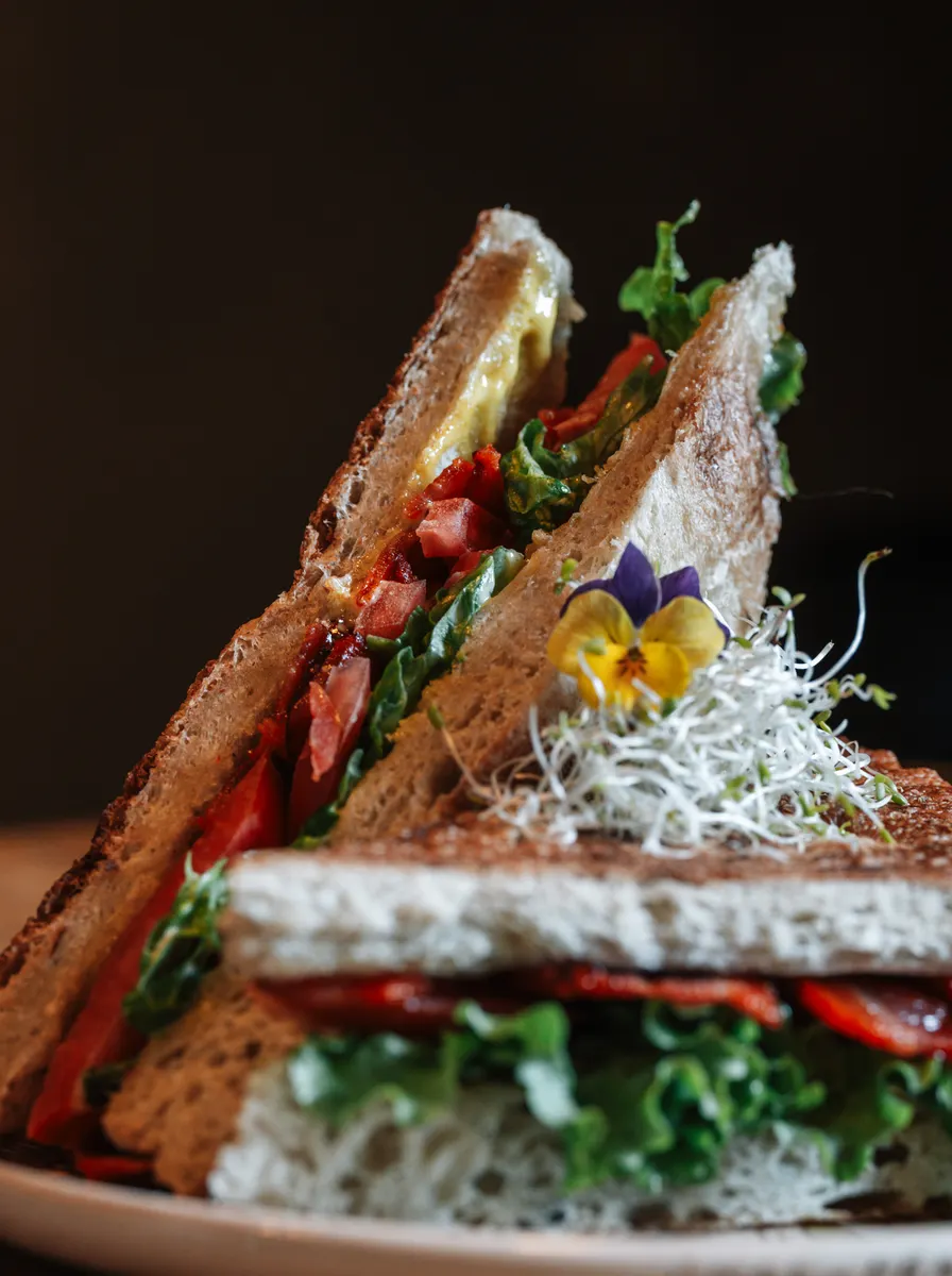 Sandwich BLT cortado en dos, con tocino crocante, lechuga y tomate, servido en plato de cerámica